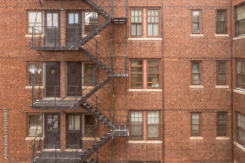 Side of vintage red brick apartment building with steel fire escape in large urban area