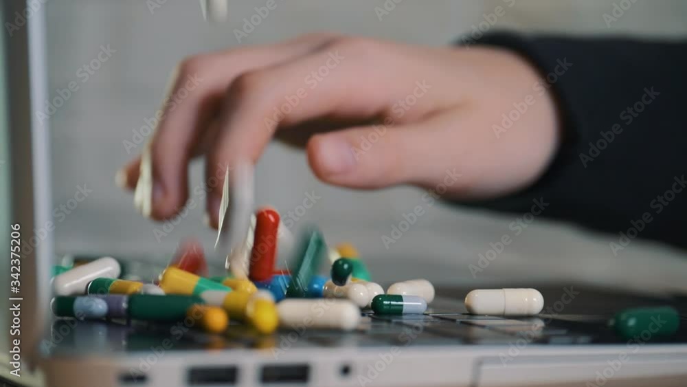 Colorful capsules, tablets falling onto the keyboard of the laptop. Human hands, women working on a laptop keyboard. Colorful capsules, tablets falling onto the keyboard of the laptop. Human hands, women working on a laptop keyboard.