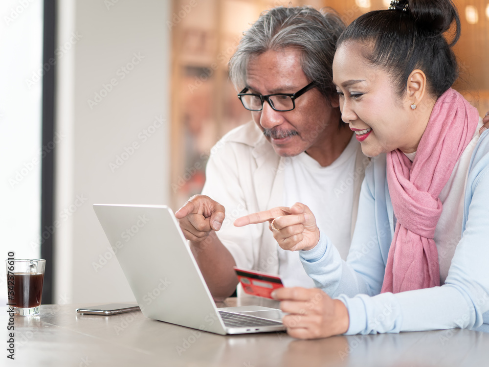 Asian senior couple using a credit card and laptop while working on their finances at home. Technology, Finance and communication Asian senior couple using a credit card and laptop while working on their finances at home. Technology, Finance and communication