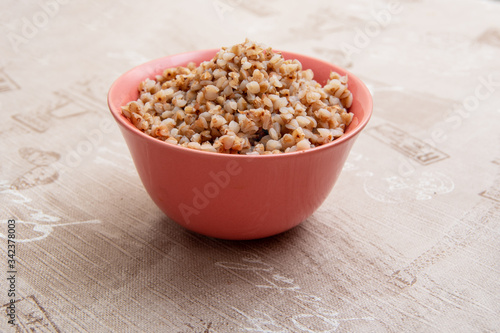 Buckwheat porridge in a pink clay bowl on the background of the kitchen table. Side view, selective focus. Russian traditional cuisine. Healthy eating concept