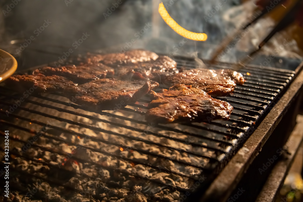 in the evening a barbecue grill on which tasty juicy steaks are grilled over an open fire, a hand holds tongs and turns the meat over. close-up, soft focus. smoke is highlighted in the evening a barbecue grill on which tasty juicy steaks are grilled over an open fire, a hand holds tongs and turns the meat over. close-up, soft focus. smoke is highlighted