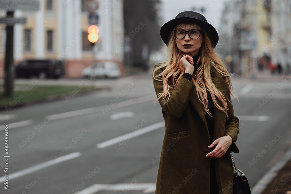 Woman wearing the glasses and black hat standing near the road and thinking
