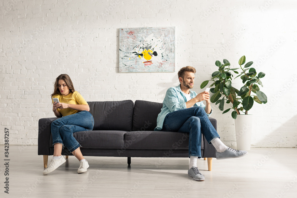 Obraz premium Young couple using smartphones on couch at home