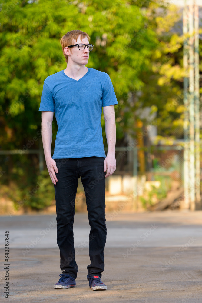 Full body shot of nerd man with red hair thinking in the park Full body shot of nerd man with red hair thinking in the park