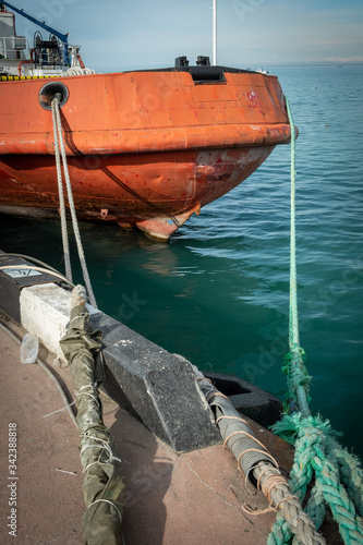 Ship on the pier. Mooring with ropes to the bollard. Red, rusty hull of the boat.