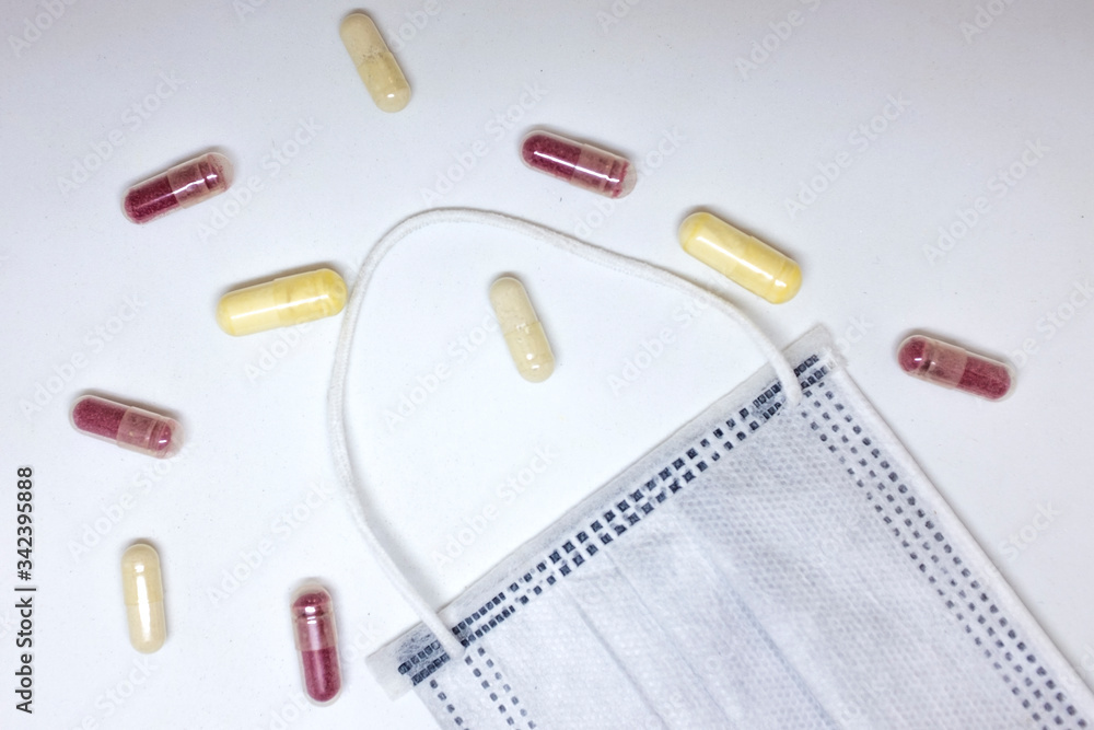 Protective white face mask to prevent fast spreading coronavirus with yellow and red pills, on white background. Protective white face mask to prevent fast spreading coronavirus with yellow and red pills, on white background.
