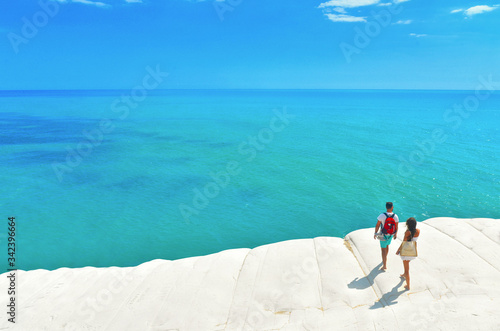 white cliffs naturally made of smooth pug at Scala dei Turchi beach with group of young people with turquoise mediterranean sea and blue cloudy summer sky near Agrigento, Sicily, Italy