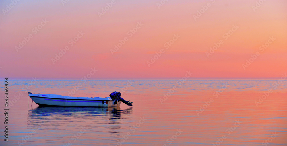 a peaceful sea with warm sunset colors and a solitary boat in a beach near Agrigento in Sicily Italy