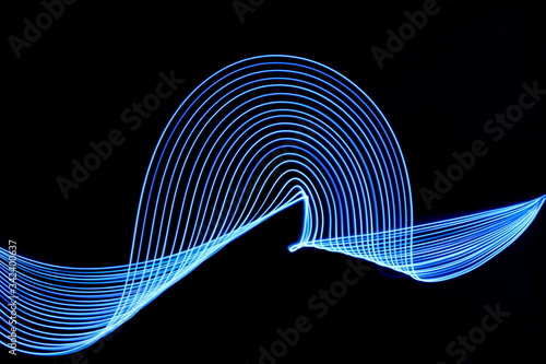 Long exposure photograph of blue neon colour in an abstract swirl, parallel lines pattern against a black background. Light painting photography.