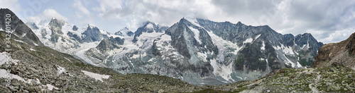 Panoramic snapshot of a ridge of snowy rocky mountains in Swiss Alps, sharp peaks are in clouds, grey stones are on foreground