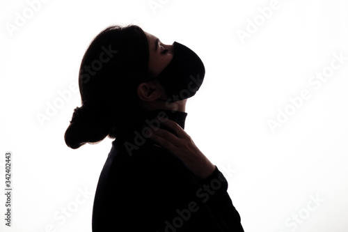 silhouette figure of young woman in protective mask on studio background  girl raised her head up with hands clasped around neck  concept health and safety