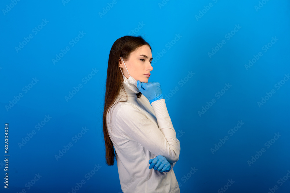 Portrait of a girl in a medical mask, which puts on a rubber glove. Blue background. Copy space. Portrait of a girl in a medical mask, which puts on a rubber glove. Blue background. Copy space.