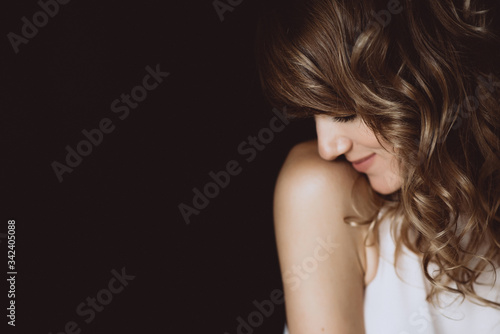 Portrait of a 36 years old woman with curly hair and brown slanting eyes looks embarrassed down. Soft selective focus.