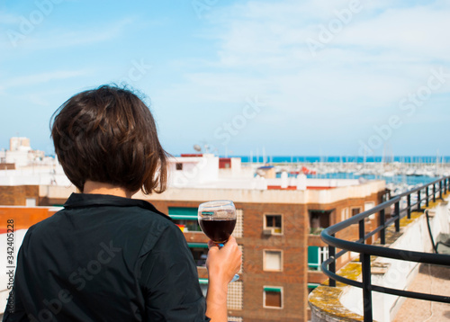 Woman look from her balcony on sea in Spain with glass of red wine. Woman in stress.