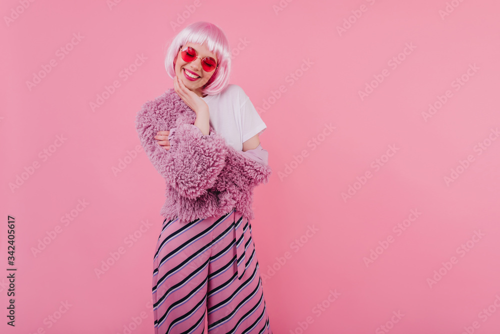 Lovely girl with short pink hair laughing with eyes closed. Studio photo of refined young lady wears peruke and trendy glasses during photoshoot.