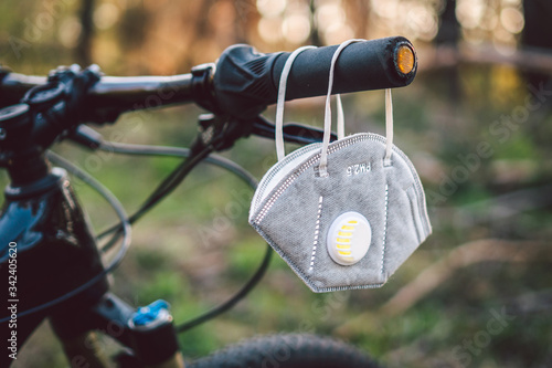 face mask, with filter pm 2.5. Flu epidemic, dust allergy, protection against virus. Covid 19 virus concept. A carbon filter respirator hangs on the handlebars of a bicycle in a forest
