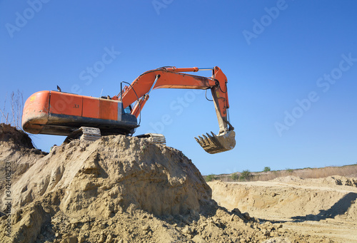 Obraz na plátně huge  crawler excavator and a construction dump truck at work on sand quarry, standing next to it while working on a sunny day against blue sky