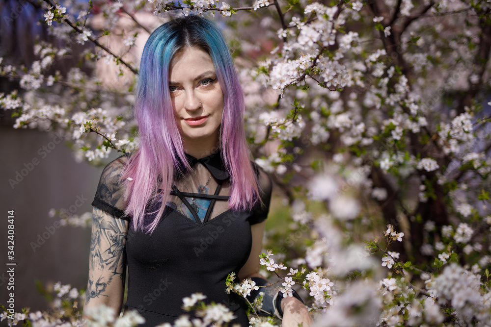 Young blue violet haired girl in black dress in a blooming garden Young blue violet haired girl in black dress in a blooming garden