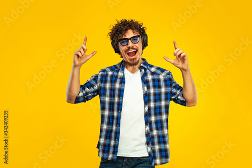Portrait of happy bearded man with curly hair pointing finger at screen isolated over yellow background. Guy in blue sunglasses and headphones pick on great idea.