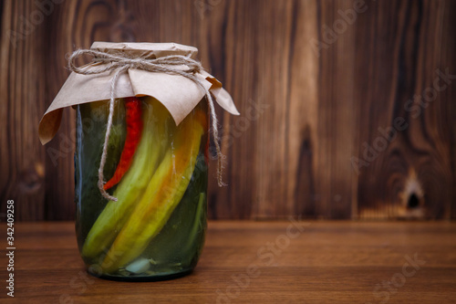 Pickled peppers in a jar on a wooden brown background, space for text. Homemade pickles.