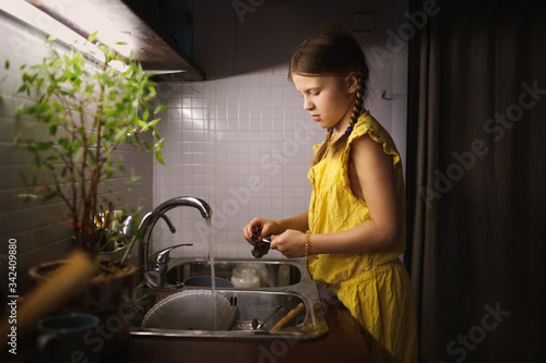 Girl child washes dishes in the kitchen sink