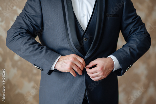 Men's hands fasten a dark three-piece business suit, close-up.