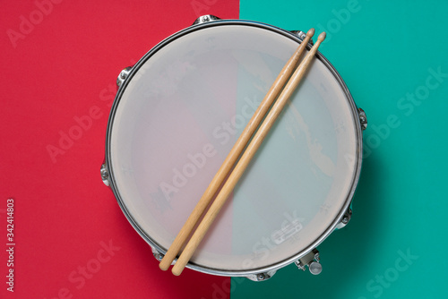 Drum and drum stick on red and green table background, top view, music concept