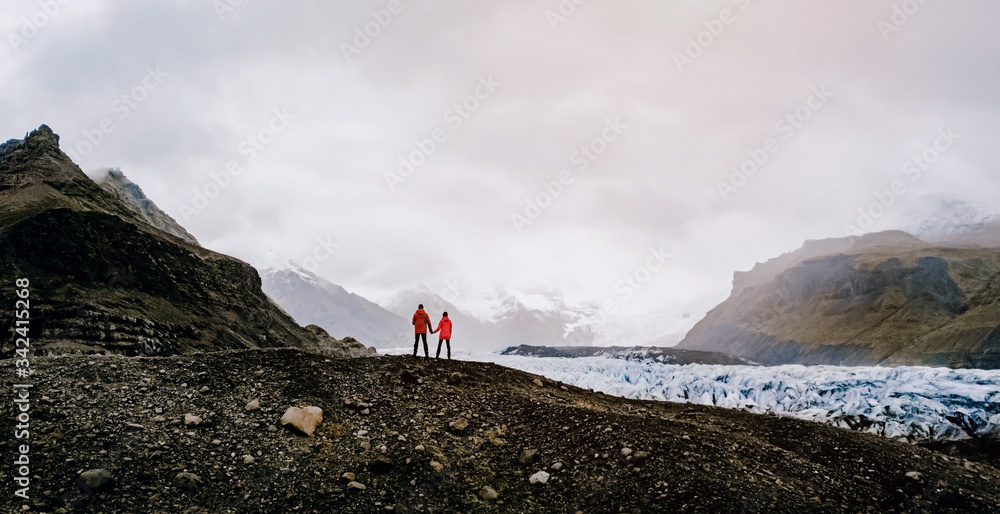 Lovely couple looks to the glacier in Iceland behind the mountains and snow. Vatnajokull National Park. Beautiful Icelandic landscape. Skaftafell and Jokulsargljufur area.