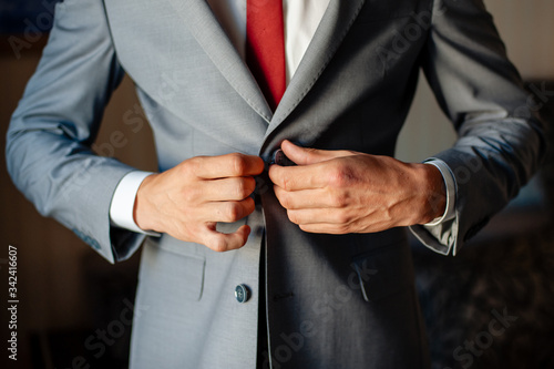 Men's hands fasten a gray business suit, close-up.
