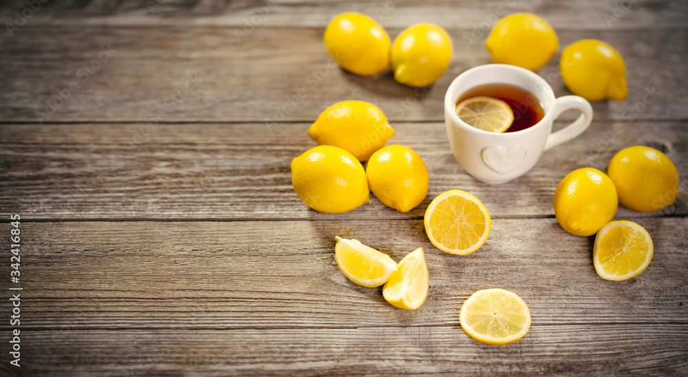 Cup of black tea with lemon slice and plenty of lemons around on grey wooden table. Warm drink infusion for cold fall and winter days. Concept of prevention for flu cold with Vitamin C Cup of black tea with lemon slice and plenty of lemons around on grey wooden table. Warm drink infusion for cold fall and winter days. Concept of prevention for flu cold with Vitamin C