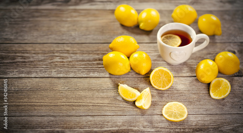 Cup of black tea with lemon slice and plenty of lemons around on grey wooden table. Warm drink infusion for cold fall and winter days. Concept of prevention for flu cold with Vitamin C
