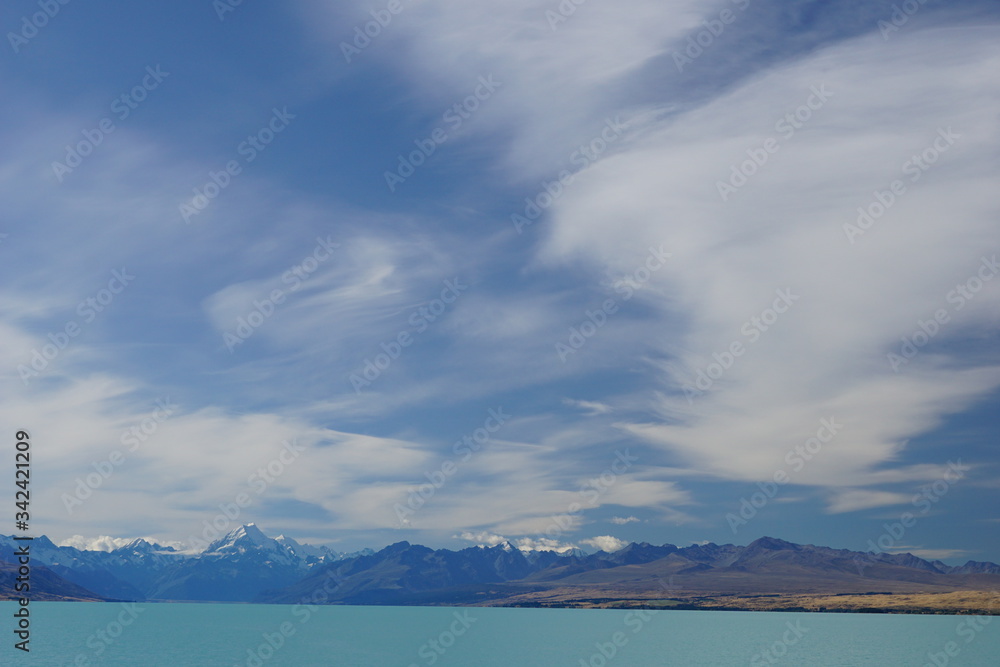 PUKAKI LAKE, NEW ZEALAND - MARCH 11, 2020: The range of Aoraki above the lake and thin clouds in the sky
