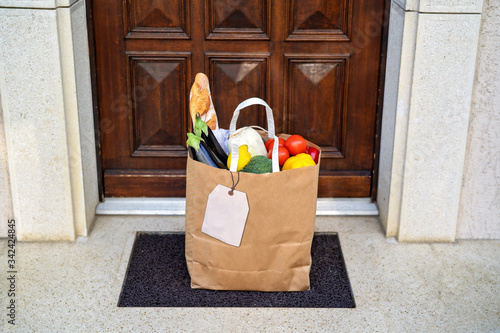 Contactless food delivery service concept. Paper bag with groceries delivered and left outside at entrance door.  Online shopping. Healthy fresh fruit and vegetables, zero waste, recyclable package.