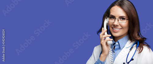 Portrait picture of happy smiling young doctor talking on phone, dark blue color background. Copy space for some sign, slogan or advertising text. Medical call center service. photo
