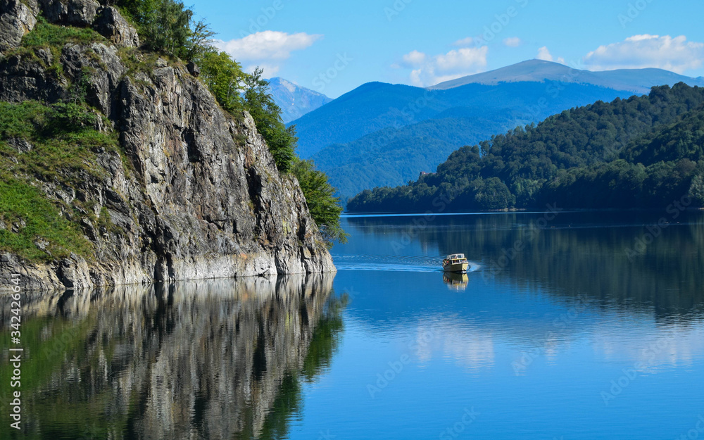 A small pleasure boat crosses the Vidraru lake (hydropower construction) in the Carpathian Mountains, Transfagarasan (Romania)