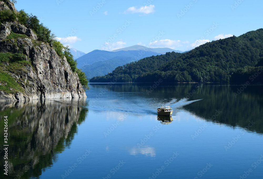 A small pleasure boat crosses the Vidraru lake (hydropower construction) in the Carpathian Mountains, Transfagarasan (Romania)