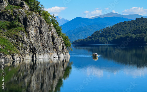 A small pleasure boat crosses the Vidraru lake (hydropower construction) in the Carpathian Mountains, Transfagarasan (Romania) © Vali