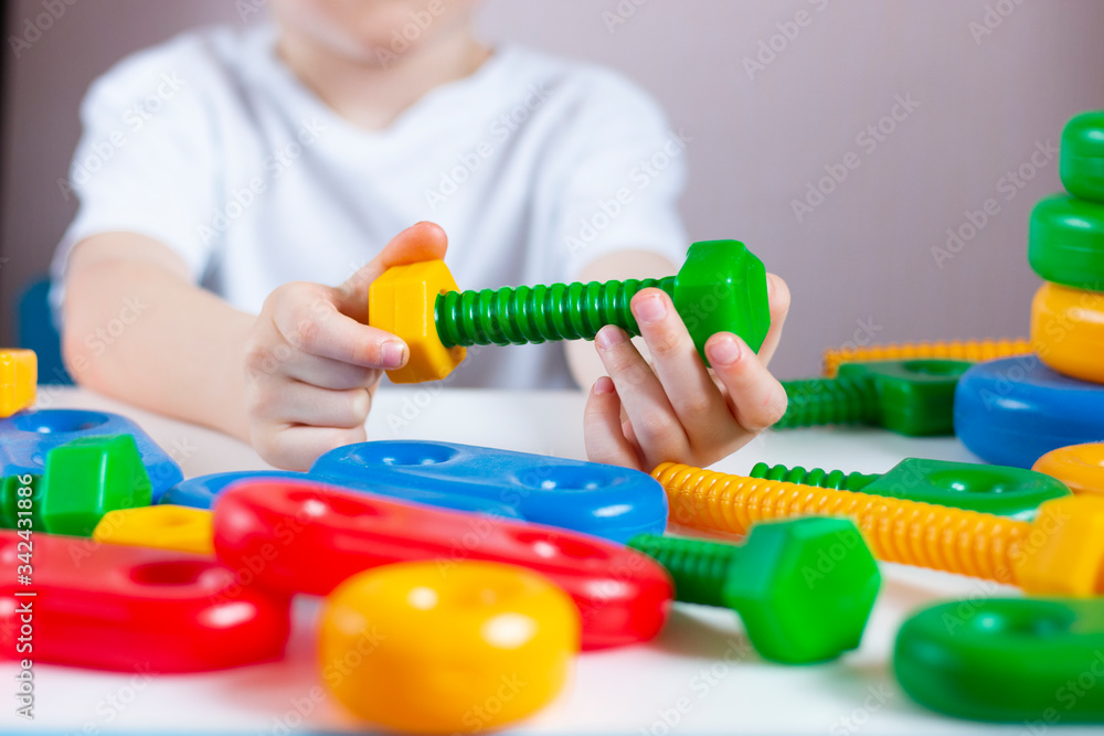 The child plays in the developmental constructor and tightens the bolt and nut. Children's creativity and learning. Home leisure. The child plays in the developmental constructor and tightens the bolt and nut. Children's creativity and learning. Home leisure.