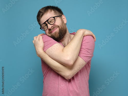 If you are single, hug yourself. Funny, cute bearded man in glasses cuddling himself and dreams with eyes closed. photo