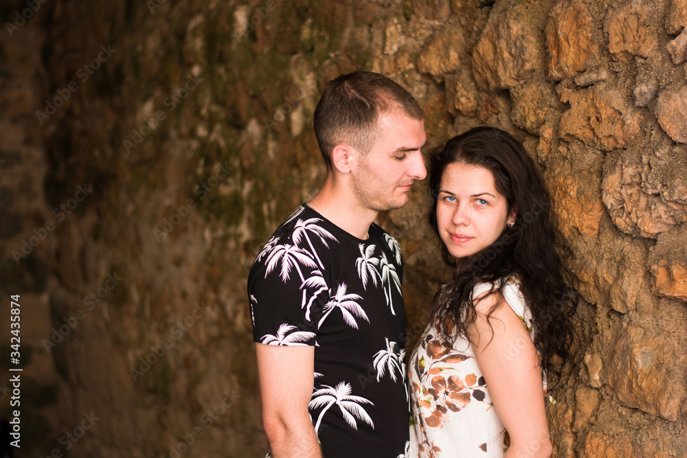 Couple in love embracing on a stone wall background, brunette femle is looking at the camera, her man looks at her with love and passion.