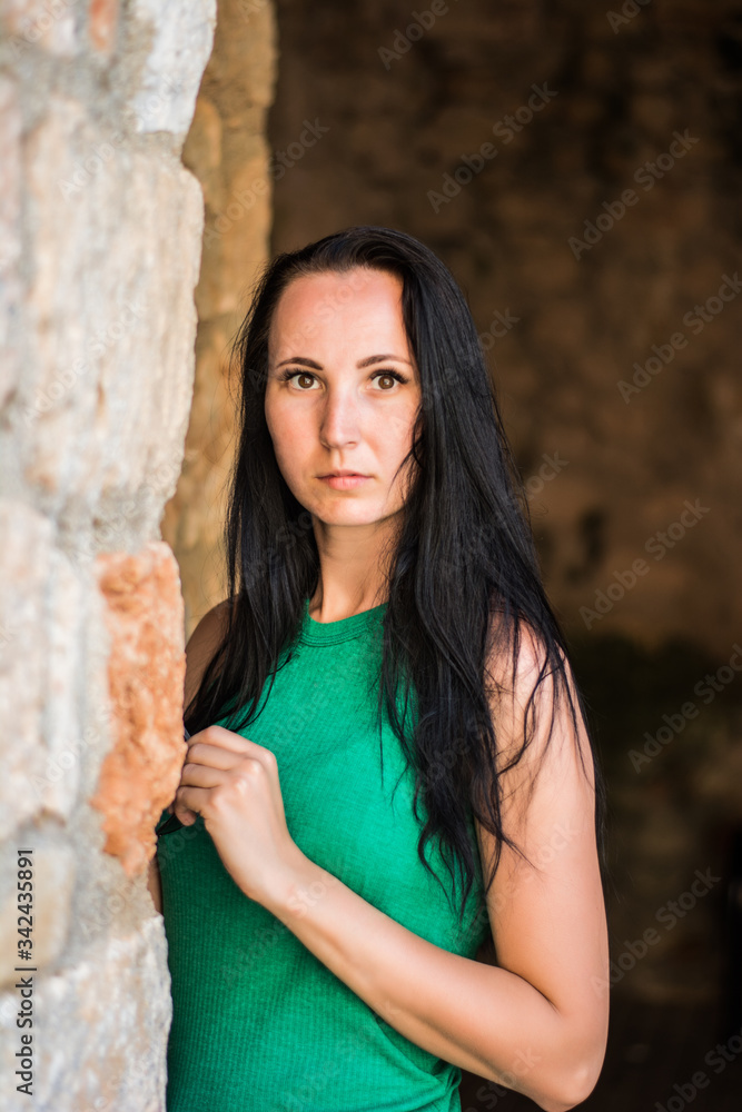 Portrait of young woman with long black hair leaning to snote wall, expressing anxiety.