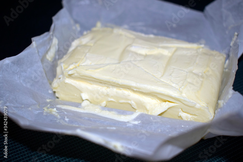 An open packet of butter on a dark green tablecloth. Dairy product in parchment packaging.