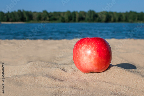 Red apple on the sand on the river beach with the sunlight