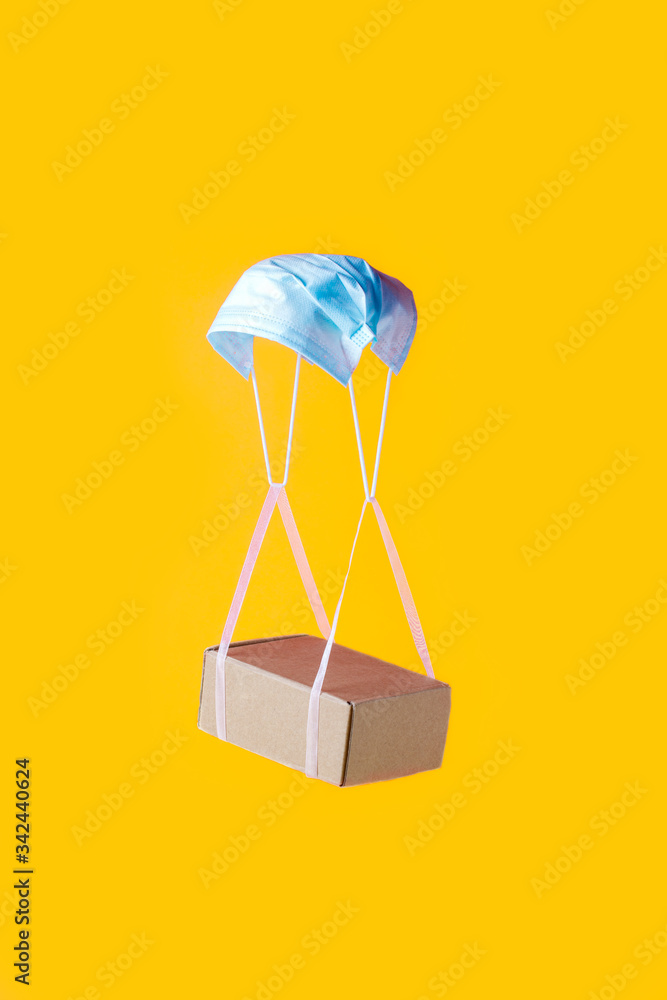 Fototapeta premium Quarantine, contactless delivery during a pandemic coronavirus covid-19. Stay at home, Online shopping, trendy color block concept, box hanging on slings and medicine face mask