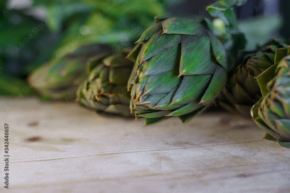 Fototapeta premium Close up of thorns leaves of the artichokes freshly picked by the farmer laid on a wooden table and illuminated by sunlight, vegan and mediterranean cuisine ingredients