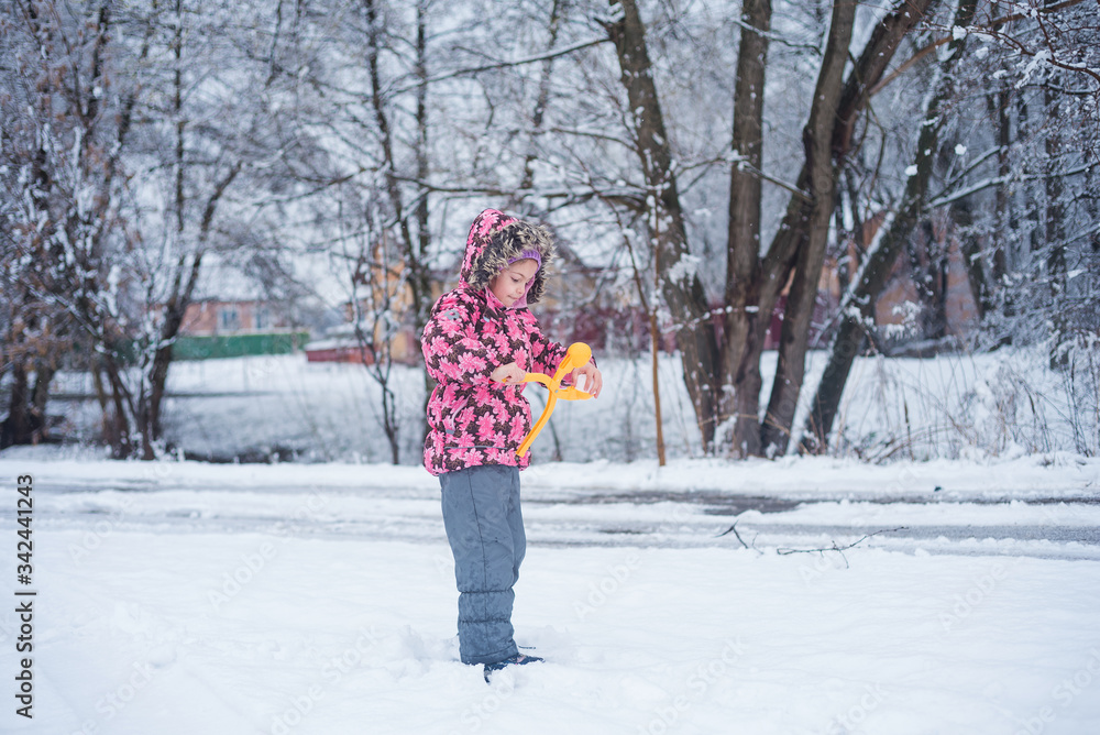 A little girl in a warm jacket and jumpsuit plays with the snow