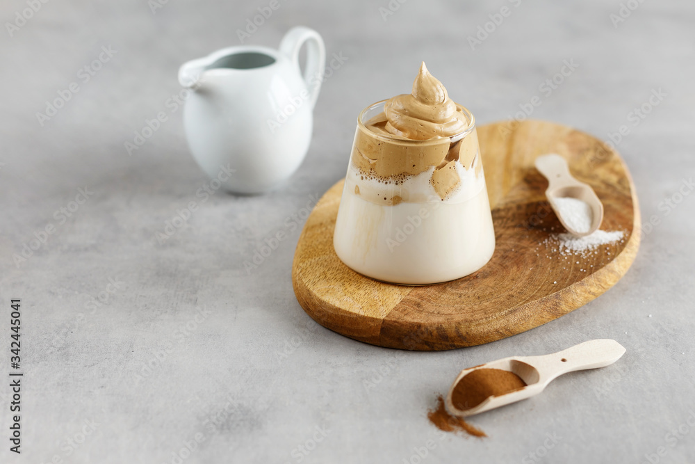 Korean drink. Homemade dalgona coffee in glass with milk on grey background. Trendy fluffy creamy whipped coffee. Wooden stand. Korean drink. Homemade dalgona coffee in glass with milk on grey background. Trendy fluffy creamy whipped coffee. Wooden stand.