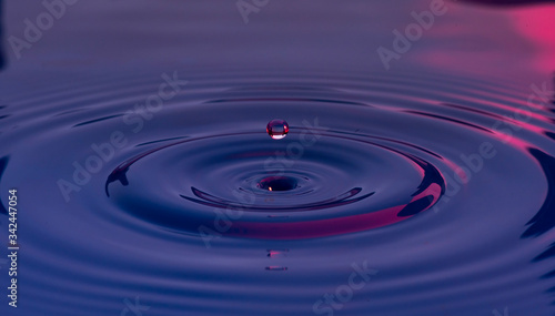 Gotas de agua color azul con morado suspendidas en el aire y formando ondas en la superficie liquida, que representan tranquilidad o serenidad