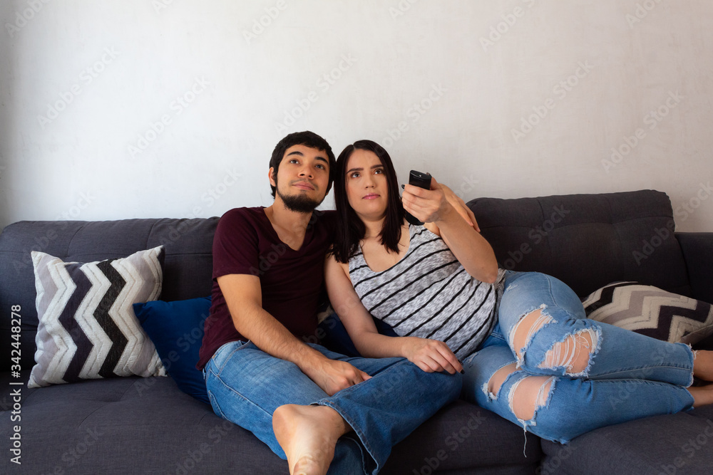 Young adult Hispanic married couple.hugging on the couch, watching TV smiling as a family Young adult Hispanic married couple.hugging on the couch, watching TV smiling as a family