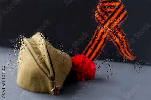 Window,rain drops.Forage,garisson cap of World War II soldier. Red star,carnation flower,St. George ribbon.May 9.Memory 75 years of victory day of Soviet Union in Great Patriotic War.Dark background photo